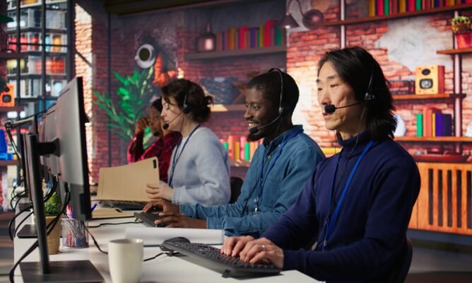 Call center operator next to coworkers dealing with upset customers, speaking using headset at office desk. Teamworking staff members doing customer support job, handling clients complaints, camera B