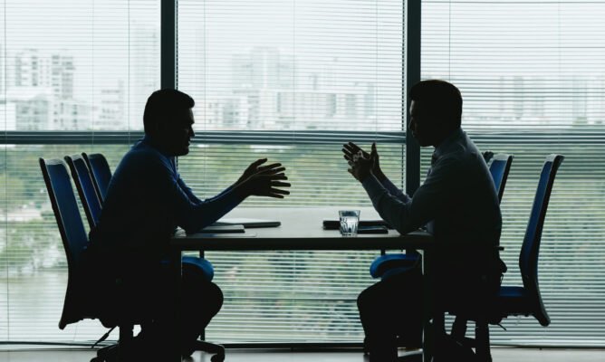 Silhouettes of business people sitting at table against the office window and discussing various issues