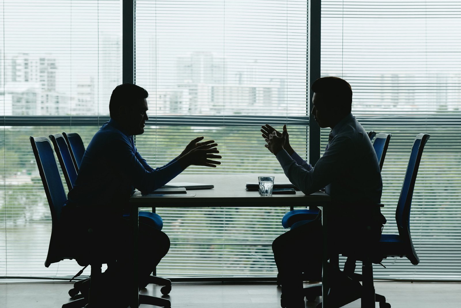 two human outlines against shuttered office window sitting opposite each other negotiating scaled