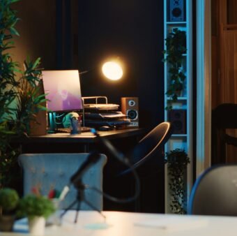 Computer screens showing running animation rendering in dimly lit empty home interior. 3D renders on digital displays in neon illuminated cozy apartment living room filled with house plants